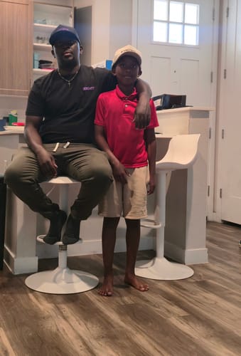 Reviewer wearing the black 80Eighty DCG89 shirt, sitting on a stool with an arm around a young boy.