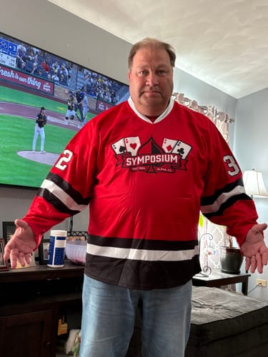Customer showing the front of their custom red hockey jersey with a 'SYMPOSIUM' logo in their living room.