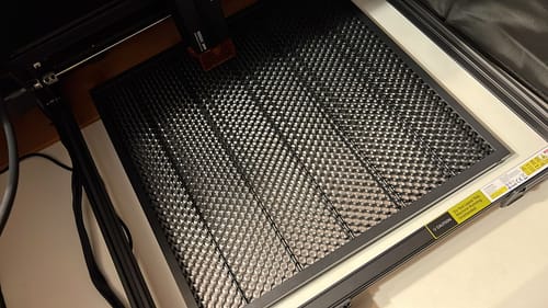 Close-up of a customer's black AtomStack F4N Honeycomb bed sitting inside a laser engraving machine frame.