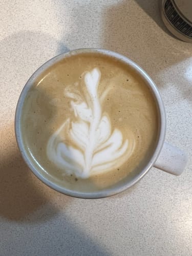 Customer's cup of coffee made from the sampler pack, with detailed white foam art on top in a light-colored mug.