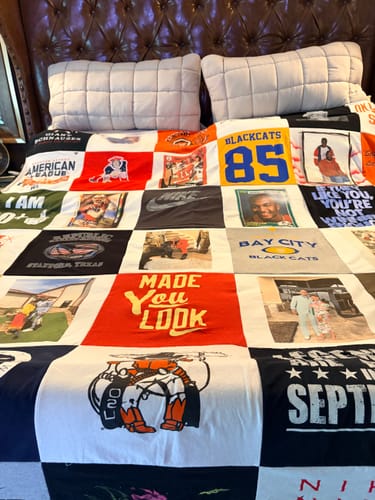 Customer's colorful Project Repat T-Shirt Quilt with many patches, spread out on a large bed.