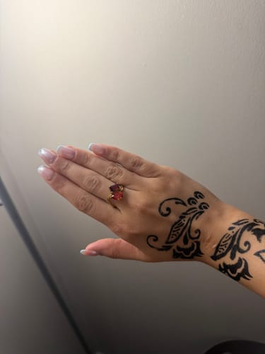 A customer's hand with henna, wearing the Navae Birthstone Ring with two red stones.