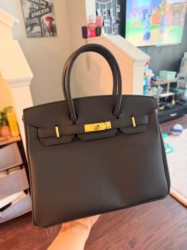 Reviewer holding a black pebbled LALUVA Warkin Bag with gold hardware in a living room.
