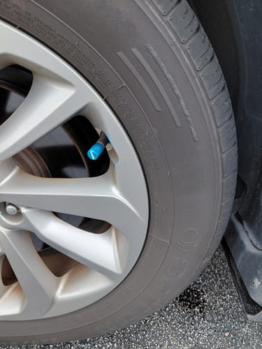 Customer's teal valve stem cap installed on a silver car wheel.