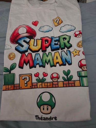 Rezensent zeigt ein personalisiertes weißes T-Shirt mit dem Aufdruck „Super Maman“ im Videospiel-Stil und dem Namen „Théandre“.