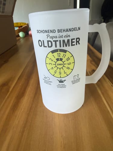 Kunde zeigt seinen matten, personalisierten OLDTIMER-Bierkrug auf einem Holztisch.