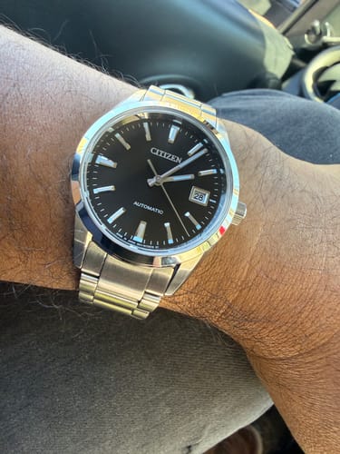 Primer plano del reloj Citizen NB1050-59E de un cliente en su muñeca, mostrando la esfera negra y la correa de acero.
