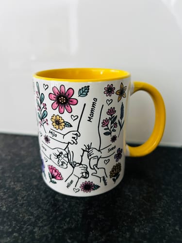 Kundens vita Kärleksmugg med ett personligt tryck av händer och blommor, placerad på en bänkskiva.