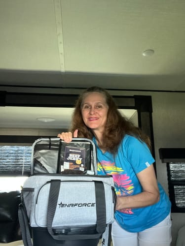A reviewer smiles while showing her open, grey Enrforce Lunch Box indoors.