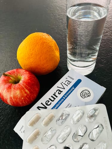 Kundenfoto der NeuraVia-Packung und des Blisters, neben einem Apfel, einer Orange und einem Glas Wasser.