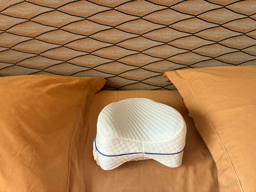 Le coussin orthopédique pour genoux Cellsius d'une cliente, posé sur un lit entre deux oreillers.