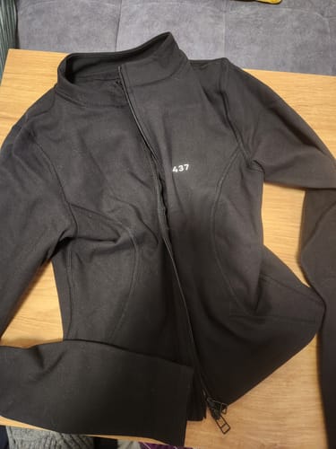 Customer's black Curve Jacket laid flat on a wooden surface, showing the zip-up front and white logo.