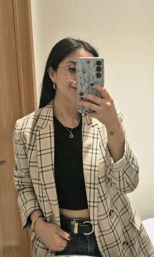 Una cliente luce el Collar Medalla con un top negro y un blazer a cuadros.