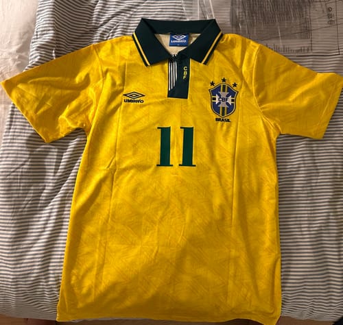 Un client présente son maillot rétro du Brésil 1993-1994 jaune avec un col vert et le numéro 11, posé à plat.