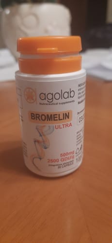 Il cliente mostra il flacone bianco di Bromelin ULTRA con tappo arancione appoggiato su un tavolo di legno.