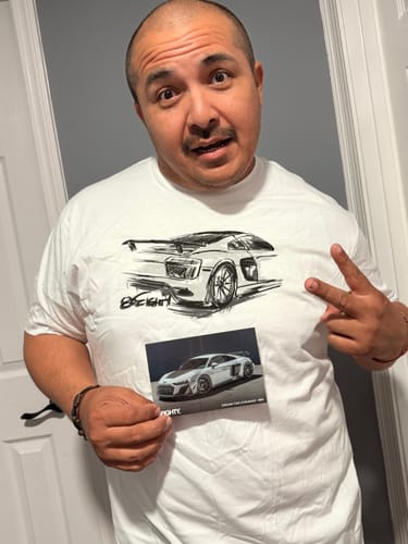Reviewer wearing the white 80Eighty Rendering Shirt, holding a car photo and making a peace sign.