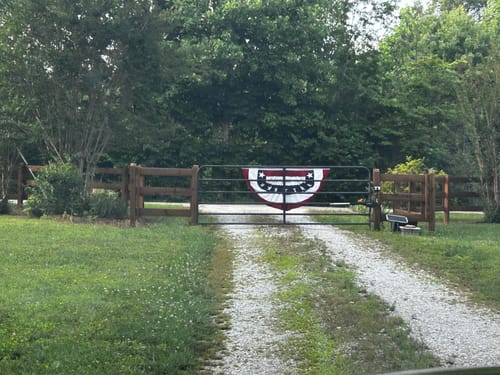 Customer's Americana Pleated Fan with Stars seen from a distance on a gate at the end of a gravel driveway.