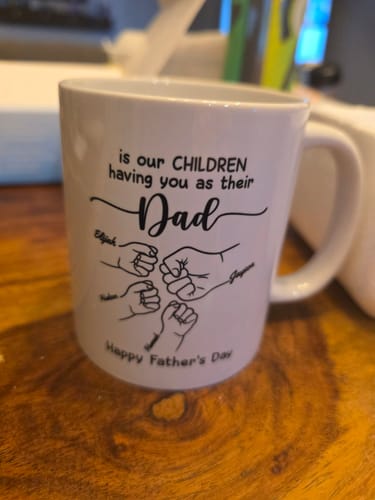 Reviewer's personalized Father's Day mug with an outlined fist bump design with names, sitting on a wooden table.