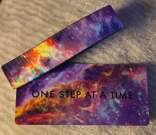Reviewer's galaxy-print wristband from the Feel-Good 3-Pack and its matching card that says "ONE STEP AT A TIME".