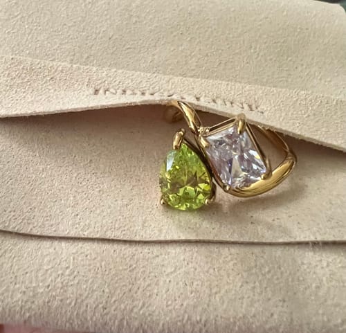 Customer's Navae Birthstone Ring with a green pear-cut and a clear radiant-cut stone, resting in a pouch.