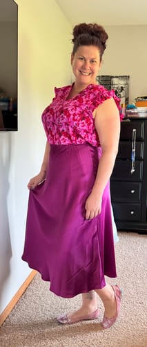 Reviewer smiling while wearing the floral Petunia Ruffle V Tank tucked into a long magenta skirt.
