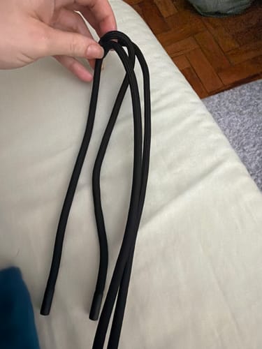Uma pessoa segurando a Cordinha Odara preta, dobrada ao meio, em sua mão sobre um fundo branco.