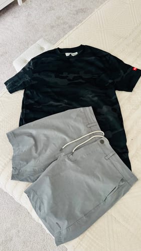 A customer's 80Eighty® BlackCamo Shirt laid out flat on a bed with a pair of grey shorts.