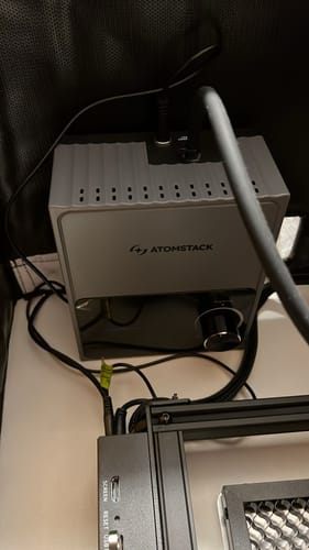 Reviewer's AtomStack F80 Air Assist unit installed and connected to a laser engraver inside an enclosure.