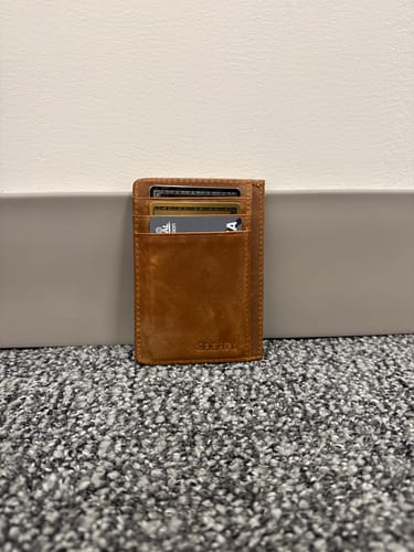 Reviewer's slim Cognac Leather Wallet filled with cards, standing on a carpeted floor against a wall.