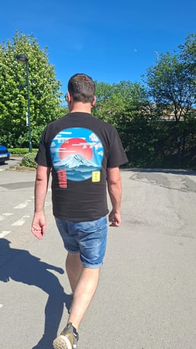Customer seen from behind walking outdoors while wearing the black Mount Fuji T-Shirt with its colorful back graphic.