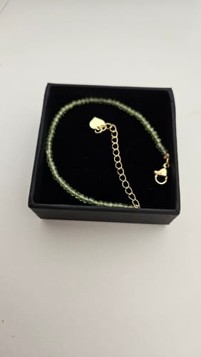Photo d'un client montrant le délicat Bracelet Péridot avec des perles vertes et un fermoir doré dans sa boîte.