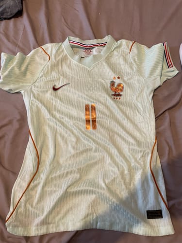 Client montrant son Maillot CDM France Vert 26/27, de couleur claire, posé à plat sur un lit.