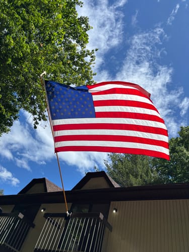 Customer's Heavy Duty American Nylon Flag waving on a pole attached to a house against a blue sky.