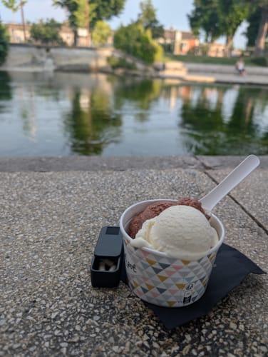Customer's open black Nano Case with pills, sitting next to a cup of gelato by the water.
