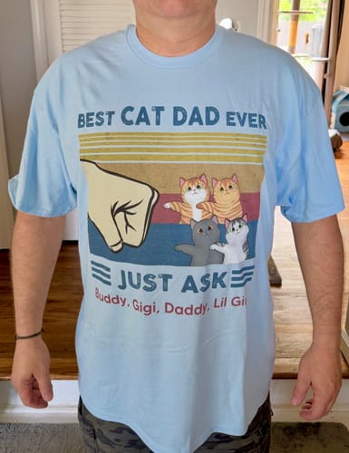 Customer wearing a light blue personalized "Best Cat Dad Ever" shirt with a fist bump graphic, four cats, and custom names below.