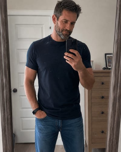 Un cliente indossa la T-shirt VARLANI blu con un paio di jeans in una foto allo specchio.