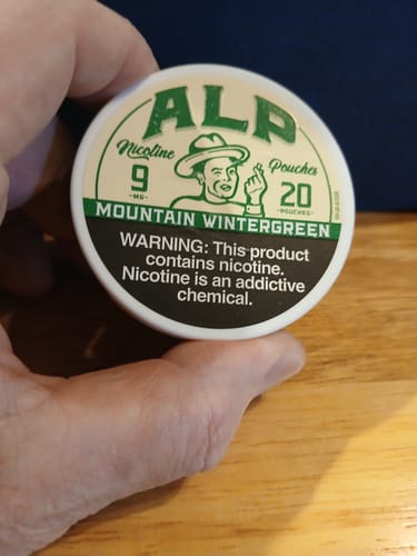 Reviewer's hand holding the white tin of ALP Mountain Wintergreen Nicotine Pouches.