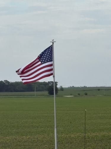 Customer's American flag flying on a flagpole in an open field.