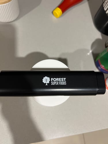Customer's black Pill Dispenser case, with a logo, resting on a white circular object on a countertop.