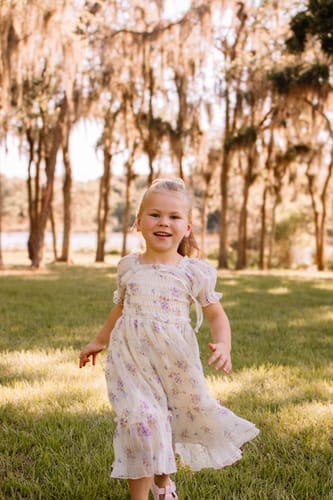 Customer's child wearing the lovely Spring Florals Dress while running in a grassy park.