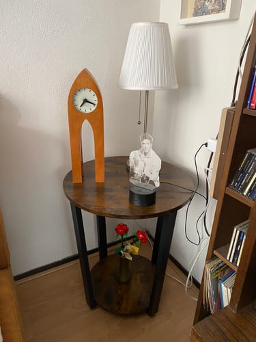 Recensent toont de ronde bijzettafel in een hoek van de kamer, gedecoreerd met een lamp en een klok.