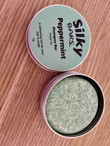 A customer's green Peppermint Shampoo Bar in its open silver travel tin, sitting on a wooden surface.