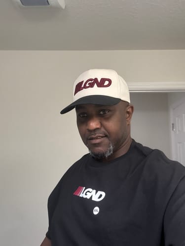 Customer wearing the cream and black Five-Panel Champ Cap with an embroidered logo.