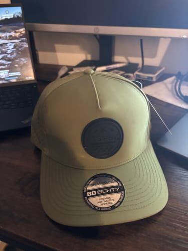 Customer's light green 80Eighty Vert Hat with a black circular patch, shown on a desk.
