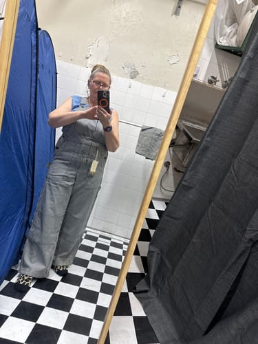 Reviewer taking a full-length mirror selfie from the front while wearing hickory stripe overalls in a fitting room.
