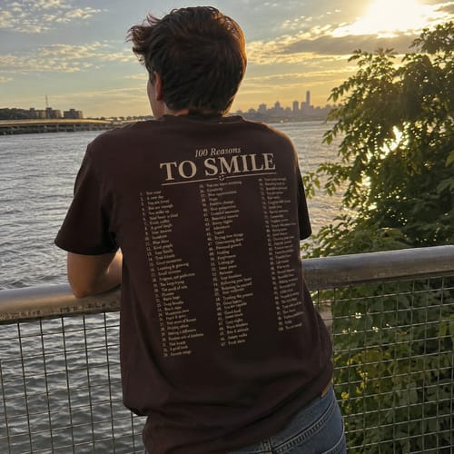 Reviewer seen from behind wearing the 100 Reasons To Smile Shirt, looking at a sunset over the water.