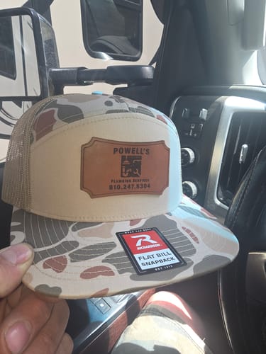 Customer holding a custom leather patch trucker hat with a camouflage flat bill and tan mesh back.