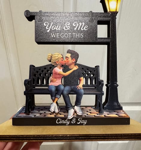 A frontal view of the reviewer's personalized wooden plaque showing a couple kissing on a bench with a lit lamppost.