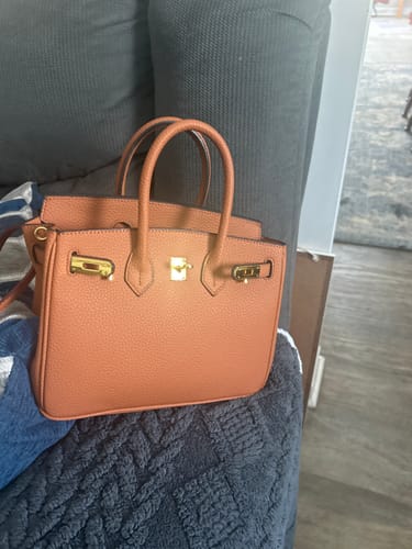 Customer's bronze pebbled leather Warkin Bag with gold lock hardware, resting on a dark gray couch.