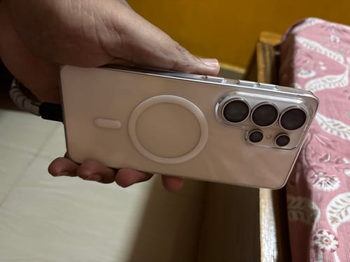 Customer's hand holding a Samsung phone in the clear Magsafe case, showing the back with camera cutout and metal buttons.